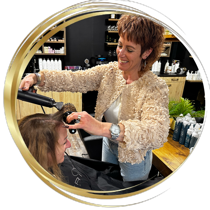 Professionele föhnbehandeling in kapsalon: kapster stylet het haar van klant met ronde borstel en föhn in een warme, moderne salonomgeving.