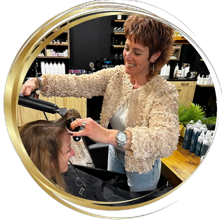 Professionele föhnbehandeling in kapsalon: kapster stylet het haar van klant met ronde borstel en föhn in een warme, moderne salonomgeving.